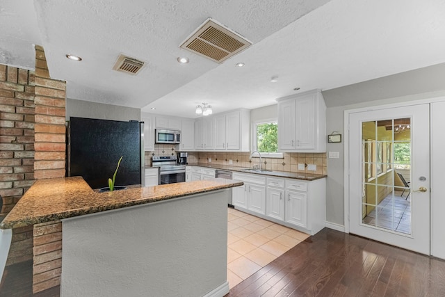 8918 James Ct, Magnolia, TX 77354 - kitchen featuring appliances with stainless steel finishes, a peninsula, light wood-style flooring, tasteful backsplash, and white cabinetry