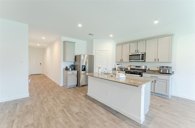 31714 Brandon Mill Trl, Fulshear, TX 77441 - kitchen featuring appliances with stainless steel finishes, light wood-style floors, light stone countertops, a kitchen island with sink, and recessed lighting
