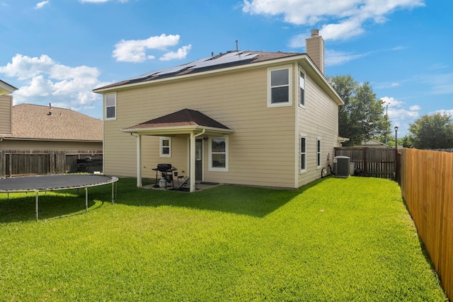 926 Seabourne Meadows Dr, Rosenberg, TX 77471 - back of house with a trampoline, roof mounted solar panels, a fenced backyard, and a chimney