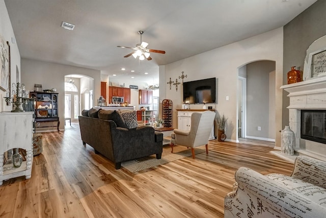 21714 Venture Park Dr, Richmond, TX 77406 - living room featuring arched walkways, light wood finished floors, ceiling fan, and a glass covered fireplace