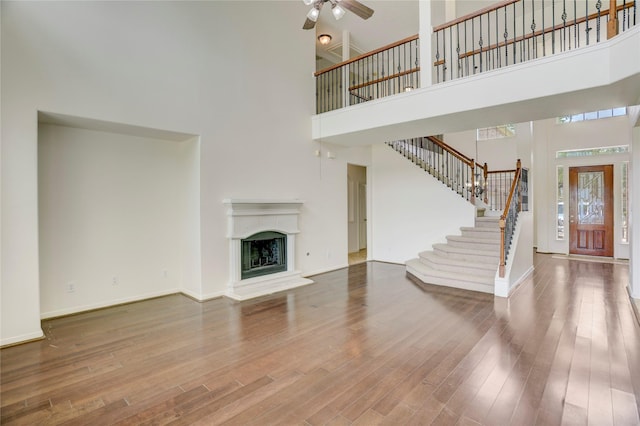 13508 Sweet Wind Ct, Pearland, TX 77584 - unfurnished living room with a towering ceiling, ceiling fan, stairs, wood finished floors, and a fireplace with raised hearth