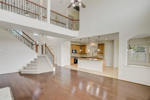 13508 Sweet Wind Ct, Pearland, TX 77584 - unfurnished living room with arched walkways, light wood-type flooring, a high ceiling, a ceiling fan, and stairs