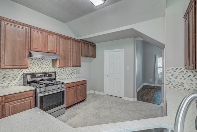 8014 Pine Wood Ct, Baytown, TX 77523 - kitchen with stainless steel gas stove, under cabinet range hood, light countertops, vaulted ceiling, and backsplash