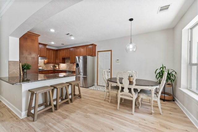 9119 Bush Buck Ln, Conroe, TX 77303 - kitchen featuring stainless steel fridge, light wood-style flooring, backsplash, dark stone counters, and brown cabinets