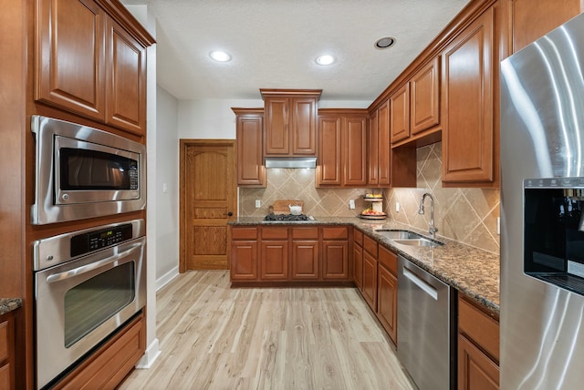 9119 Bush Buck Ln, Conroe, TX 77303 - kitchen featuring appliances with stainless steel finishes, light wood-style floors, dark stone countertops, brown cabinets, and recessed lighting