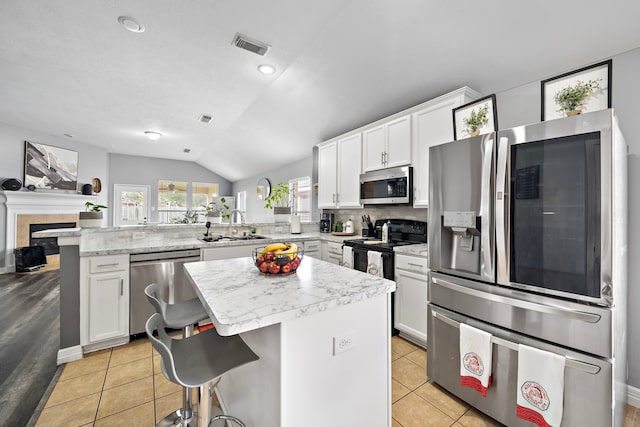 1727 Caldbeck Ln, Fresno, TX 77545 - kitchen featuring appliances with stainless steel finishes, a peninsula, vaulted ceiling, white cabinetry, and a fireplace