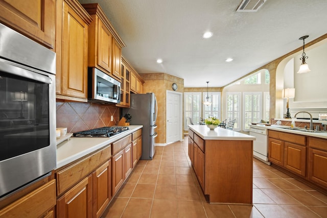 3207 Summerwind Ct, Pearland, TX 77584 - kitchen with stainless steel appliances, a kitchen island, brown cabinetry, tasteful backsplash, and recessed lighting