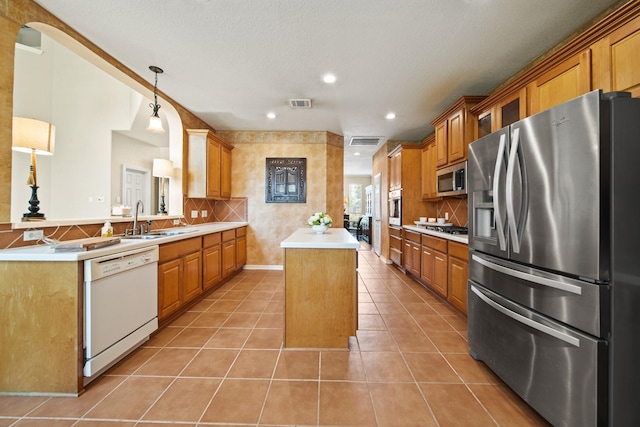 3207 Summerwind Ct, Pearland, TX 77584 - kitchen featuring stainless steel appliances, a center island, light tile patterned floors, light countertops, and brown cabinets