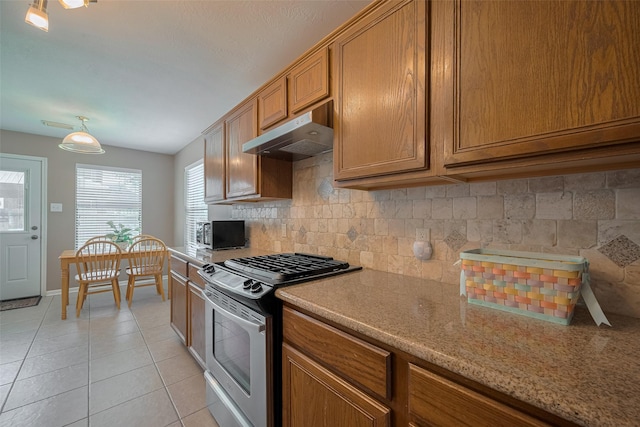 21619 Oakcreek Ct, Katy, TX 77450 - kitchen featuring stainless steel gas range oven, under cabinet range hood, brown cabinets, tasteful backsplash, and light tile patterned floors