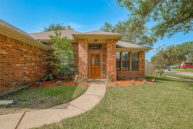 21619 Oakcreek Ct, Katy, TX 77450 - view of exterior entry with brick siding, a lawn, and a shingled roof