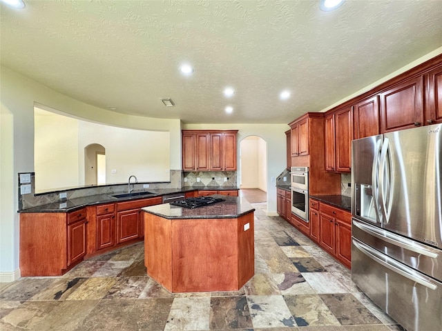 8110 Hideaway Run Way, Spring, TX 77389 - kitchen featuring arched walkways, stainless steel appliances, a kitchen island, decorative backsplash, and light stone finish floors