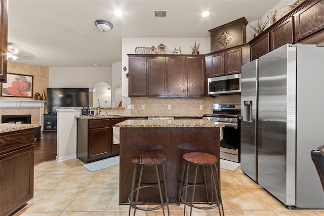 423 Carson Ridge Dr, Spring, TX 77386 - kitchen featuring appliances with stainless steel finishes, a center island, dark brown cabinets, light tile patterned flooring, and backsplash