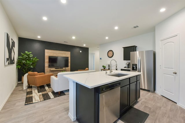 14417 Gray Rocks Rd, Splendora, TX 77372 - kitchen featuring appliances with stainless steel finishes, light wood finished floors, recessed lighting, a center island with sink, and light stone countertops