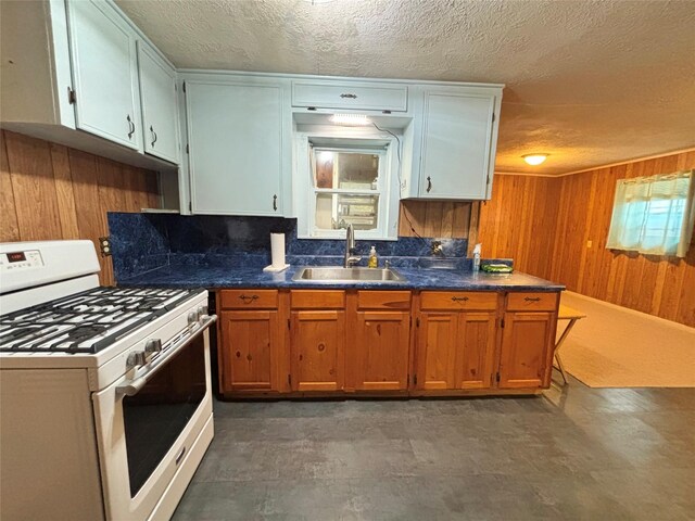 1410 W Pavillion St, Woodville, TX 75979 - kitchen with gas range gas stove, a textured ceiling, wood walls, dark countertops, and brown cabinetry