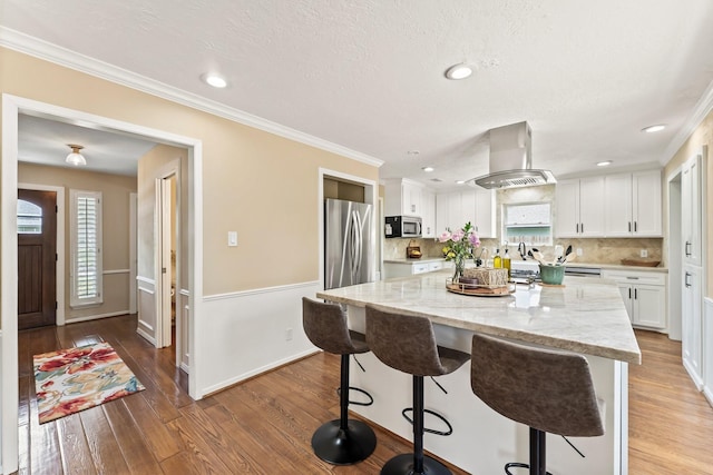115 Heather Ln, Conroe, TX 77385 - kitchen featuring island exhaust hood, appliances with stainless steel finishes, white cabinets, a breakfast bar area, and light wood-style floors