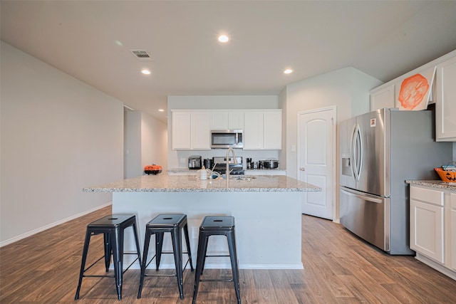 4315 Isoletta Ct, Katy, TX 77449 - kitchen with appliances with stainless steel finishes, white cabinets, wood finished floors, an island with sink, and a breakfast bar area
