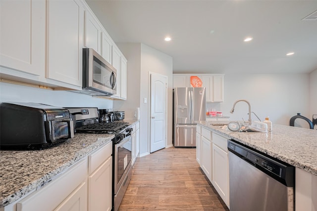 4315 Isoletta Ct, Katy, TX 77449 - kitchen featuring appliances with stainless steel finishes, light wood finished floors, white cabinets, recessed lighting, and light stone counters