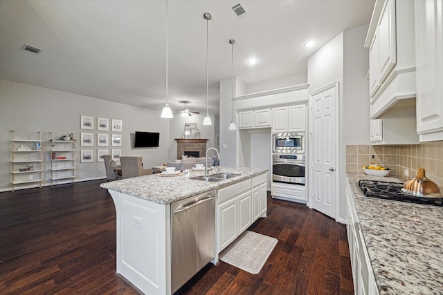 3030 Rabbit Brush Ln, Manvel, TX 77578 - kitchen with stainless steel appliances, a brick fireplace, dark wood-style flooring, white cabinets, and open floor plan