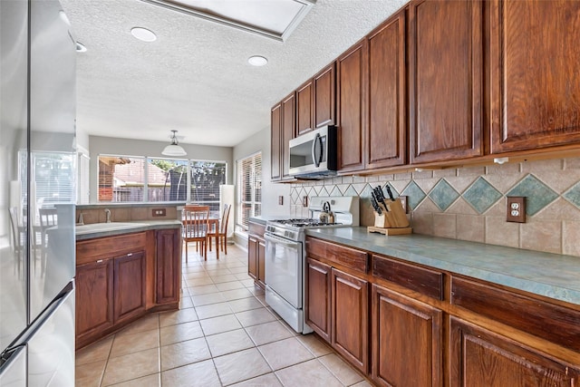 18618 Atascocita Forest Dr, Humble, TX 77346 - kitchen featuring appliances with stainless steel finishes, decorative backsplash, a textured ceiling, light tile patterned flooring, and brown cabinets