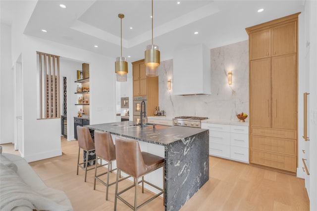 5602 Ella Lee Ln, Houston, TX 77056 - kitchen with recessed lighting, light wood-type flooring, a kitchen island with sink, a kitchen breakfast bar, and a raised ceiling