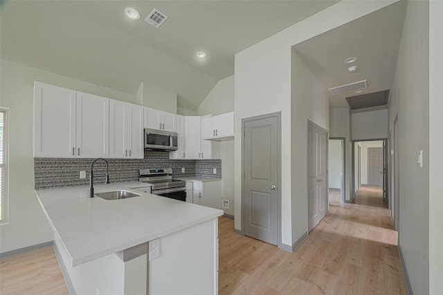 1909 Oregon St, Baytown, TX 77520 - kitchen featuring stainless steel appliances, a peninsula, light wood-style floors, decorative backsplash, and vaulted ceiling