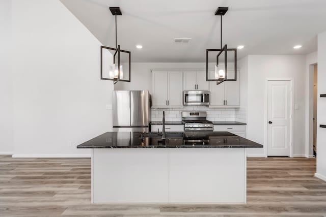 8722 Riverton Ridge Rd, Cypress, TX 77433 - kitchen with stainless steel appliances, dark stone countertops, tasteful backsplash, light wood finished floors, and an island with sink