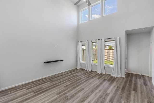 8722 Riverton Ridge Rd, Cypress, TX 77433 - unfurnished living room featuring wood finished floors, a ceiling fan, a high ceiling, and healthy amount of natural light