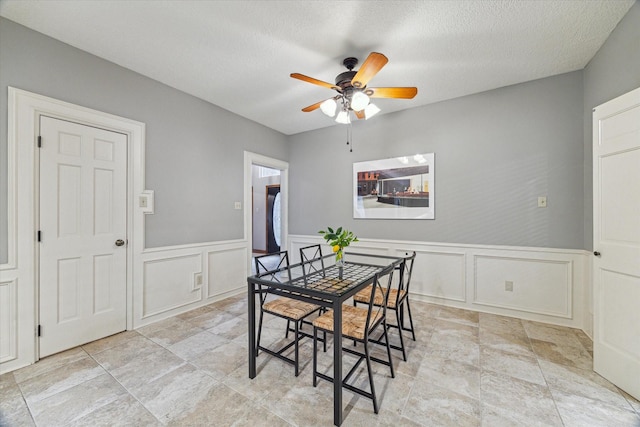 6019 Oak Creek Ln, Spring, TX 77379 - dining space with a ceiling fan, light stone finish floors, a decorative wall, wainscoting, and a textured ceiling
