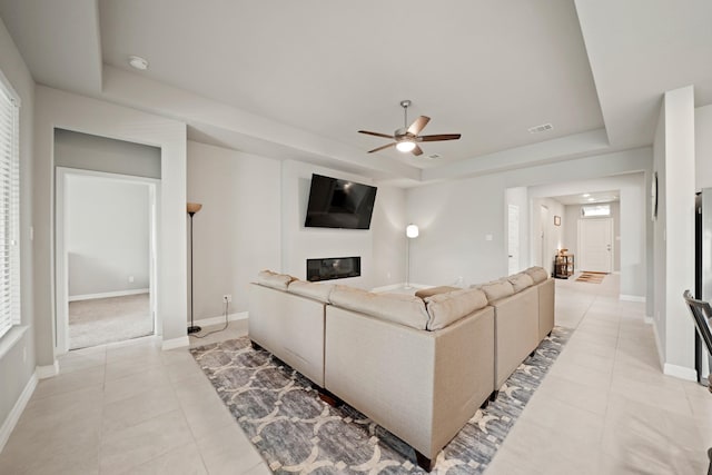 2849 Terrace Grove Dr, Conroe, TX 77304 - living area featuring a raised ceiling, a glass covered fireplace, light tile patterned flooring, and a ceiling fan