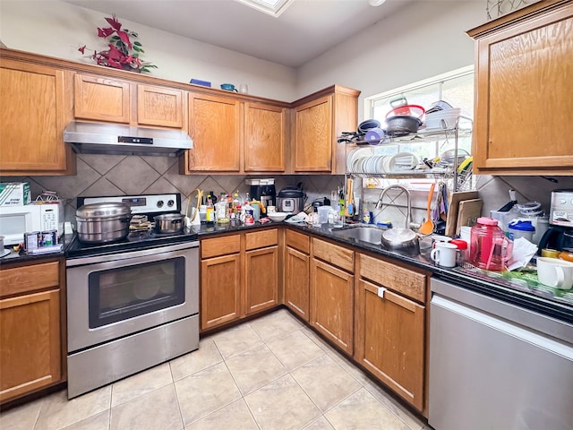 21307 Walden Grove Ln, Katy, TX 77450 - kitchen with under cabinet range hood, appliances with stainless steel finishes, decorative backsplash, light tile patterned floors, and dark countertops