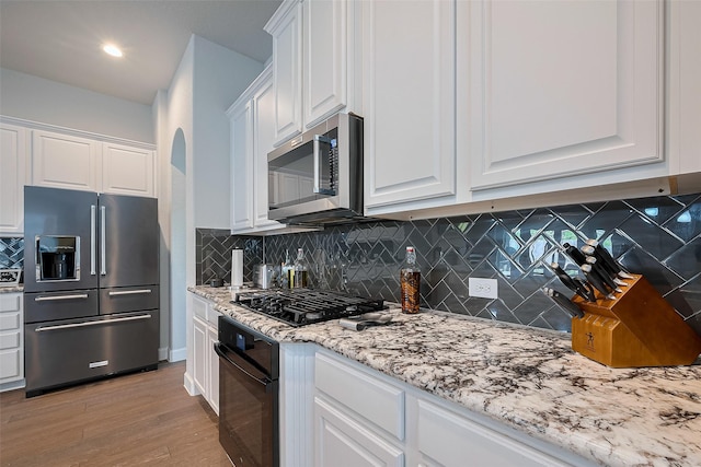 7707 Leighton Trl, Pasadena, TX 77505 - kitchen with black appliances, white cabinetry, light wood-style floors, light stone countertops, and arched walkways