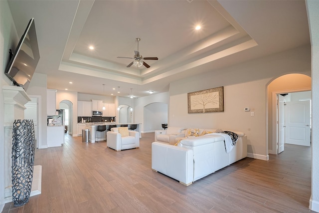 7707 Leighton Trl, Pasadena, TX 77505 - living area featuring arched walkways, a tray ceiling, ceiling fan, light wood-style flooring, and recessed lighting
