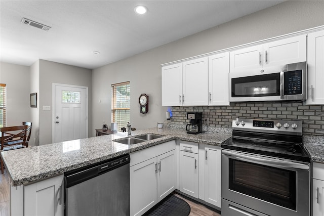 16887 Balmoral St, Montgomery, TX 77316 - kitchen featuring appliances with stainless steel finishes, a peninsula, light wood-type flooring, white cabinetry, and decorative backsplash