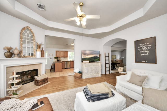 70 N Lace Arbor Dr, The Woodlands, TX 77382 - living room featuring arched walkways, light wood finished floors, a tray ceiling, ceiling fan, and a tiled fireplace