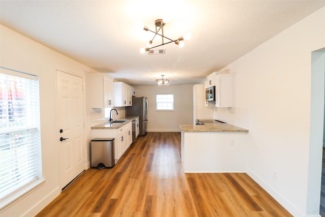 2120 Yates St, Houston, TX 77020 - kitchen with a chandelier, appliances with stainless steel finishes, light wood-style floors, white cabinets, and light stone countertops