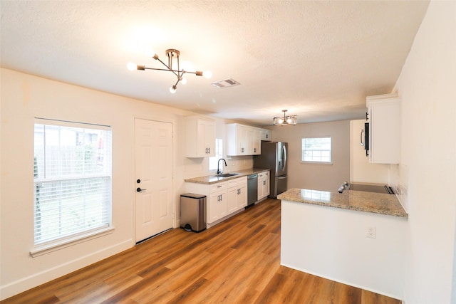 2120 Yates St, Houston, TX 77020 - kitchen featuring a chandelier, appliances with stainless steel finishes, light wood-style flooring, white cabinetry, and a textured ceiling