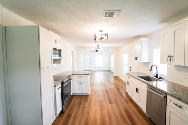 2120 Yates St, Houston, TX 77020 - kitchen with appliances with stainless steel finishes, wood finished floors, white cabinetry, backsplash, and a textured ceiling