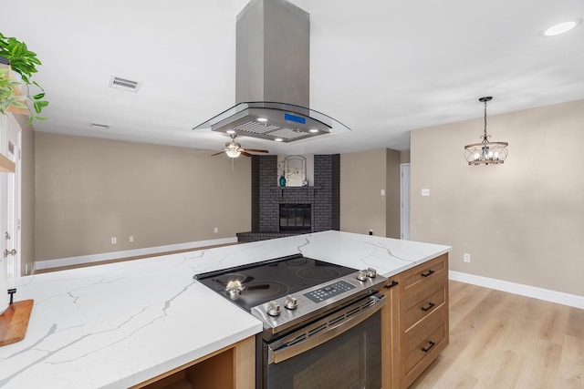 2807 Canary Ln, Humble, TX 77396 - kitchen with stainless steel range with electric cooktop, island range hood, ceiling fan, a brick fireplace, and light wood-style floors