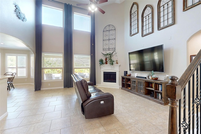 17315 Cumberland Park Ln, Humble, TX 77346 - tiled living room with arched walkways, a high ceiling, a ceiling fan, and a fireplace with raised hearth