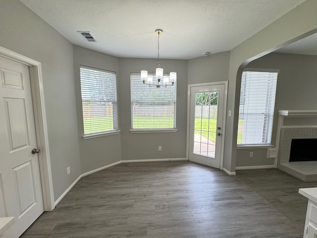 4607 Blue Rose Cir, Missouri City, TX 77459 - unfurnished dining area with wood finished floors, a chandelier, a brick fireplace, a textured ceiling, and arched walkways