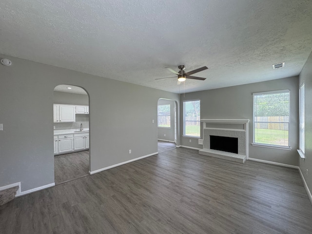4607 Blue Rose Cir, Missouri City, TX 77459 - unfurnished living room with arched walkways, a textured ceiling, dark wood-style floors, a ceiling fan, and a brick fireplace