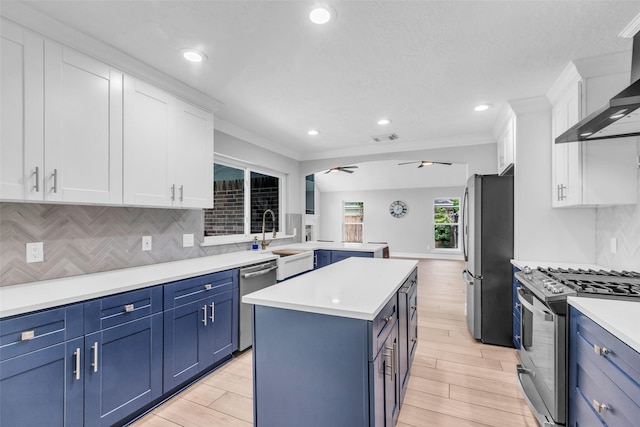 2504 Leroy St, Pearland, TX 77581 - kitchen featuring wall chimney range hood, appliances with stainless steel finishes, blue cabinets, white cabinetry, and crown molding