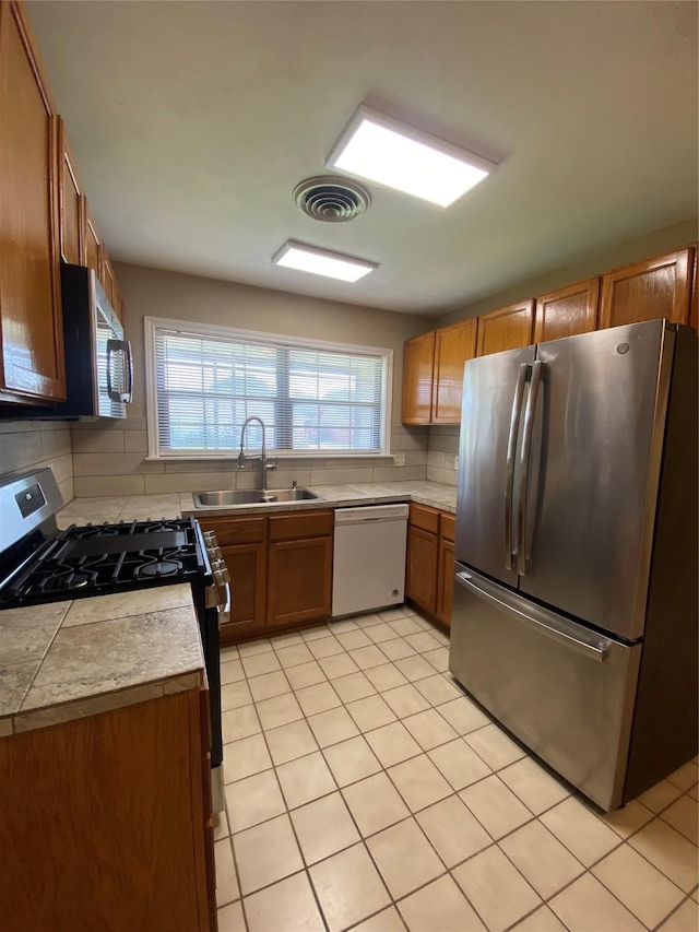 2512 Pine St, Galveston, TX 77551 - kitchen with appliances with stainless steel finishes, tasteful backsplash, brown cabinets, and light tile patterned flooring