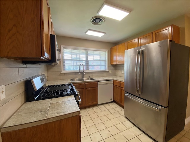 2512 Pine St, Galveston, TX 77551 - kitchen featuring appliances with stainless steel finishes, brown cabinets, tasteful backsplash, light tile patterned flooring, and tile countertops
