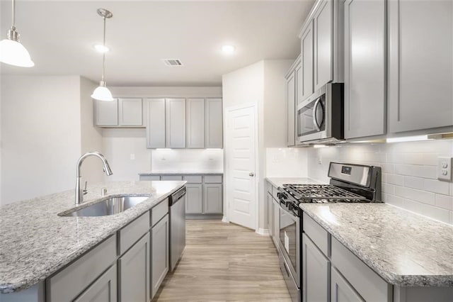 828 Laguna Green Ln, Katy, TX 77493 - kitchen with stainless steel appliances, gray cabinets, light wood-style flooring, decorative backsplash, and a kitchen island with sink