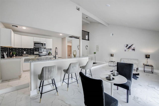 12102 Benmore Dr, Houston, TX 77099 - kitchen with stainless steel appliances, light marble finish floors, a breakfast bar, vaulted ceiling, and white cabinets