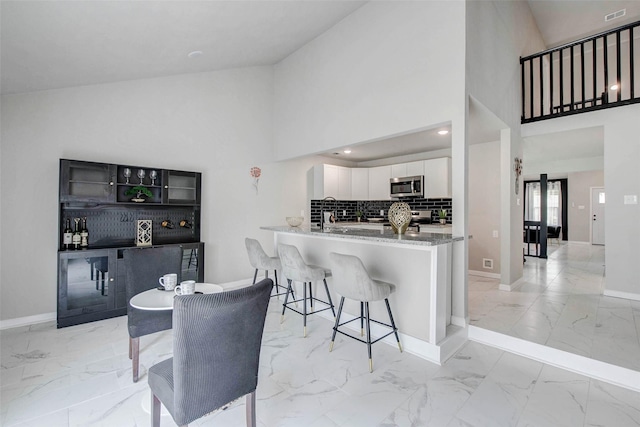 12102 Benmore Dr, Houston, TX 77099 - kitchen featuring stainless steel microwave, light marble finish floors, white cabinets, a kitchen breakfast bar, and light stone countertops