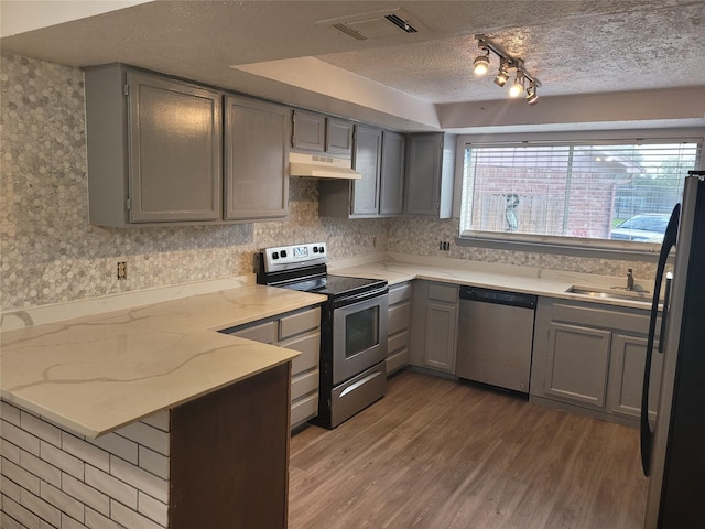 13930 New Village Ln, Sugar Land, TX 77498 - kitchen with stainless steel appliances, under cabinet range hood, gray cabinetry, a peninsula, and a textured ceiling