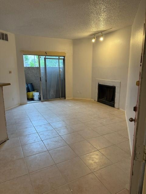 10855 Meadowglen Ln Unit 904, Houston, TX 77042 - unfurnished living room featuring light tile patterned flooring, a tile fireplace, a textured ceiling, and track lighting