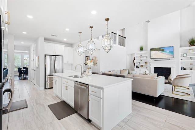 4710 Pecos Ridge Ln, Sugar Land, TX 77479 - kitchen featuring appliances with stainless steel finishes, light countertops, an island with sink, white cabinetry, and a fireplace